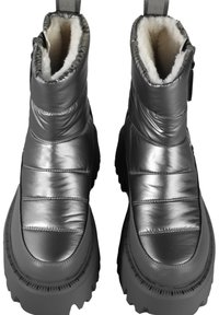 Paire de bottes d’hiver argent métallisé avec semelles noires épaisses et doublure polaire blanche visible en haut, vue de dessus.