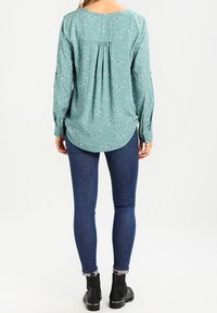 Blusa teal con un motivo floreale, maniche lunghe e orlo curvo. Abbinata a jeans skinny blu scuro e stivali neri alla caviglia.