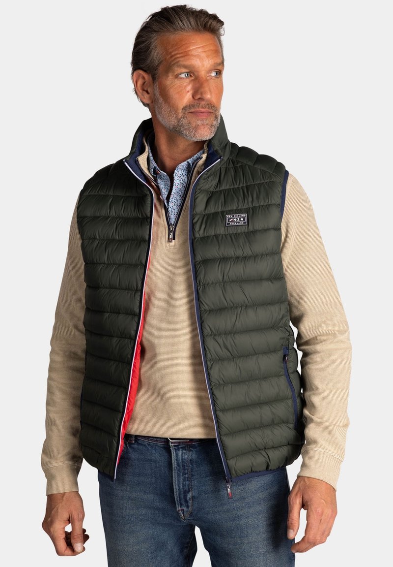 Donkergroene puffervest met ritssluiting, ontworpen met een marineblauwe bies en rode voering. Heeft een gewatteerde textuur en zijzakken.