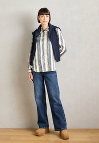 Langermet stripet skjorte i krem, blå og marineblå; brukt med en marineblå strikkegenser; løstsittende blå denimjeans; lysebrune platåsko.