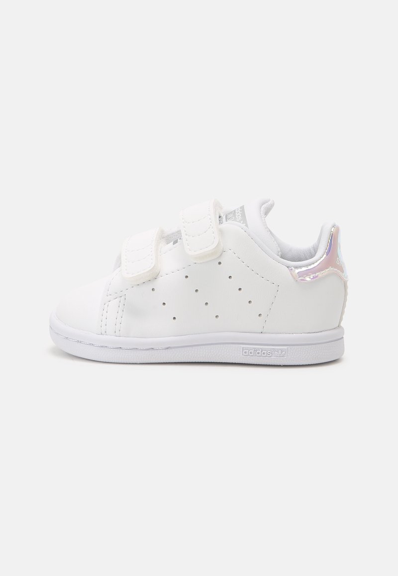 White sneaker with two Velcro straps, perforated sides, smooth synthetic upper, iridescent heel accent, and rubber sole.