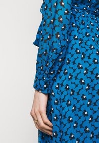 Vestido floral azul hecho de tela suave, con flores negras y acentos blancos, mangas largas y detalle de botones en los puños.