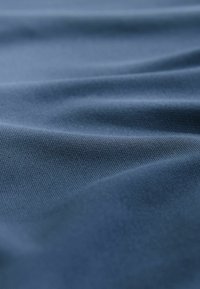 Tkanina tekstylna w ciemnym niebieskim kolorze, gładka w dotyku z delikatnym połyskiem, ukazująca łagodne fałdy i lekko prążkowany wzór na całej powierzchni.