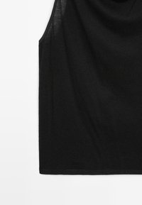 Top senza maniche di colore nero realizzato in morbido cotone, con scollatura rotonda e vestibilità rilassata. L'orlo è dritto e si trova all'altezza dei fianchi.