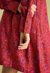 Red floral dress made from lightweight fabric features pink floral patterns, gathered sleeves, and pleated detailing at the waist.