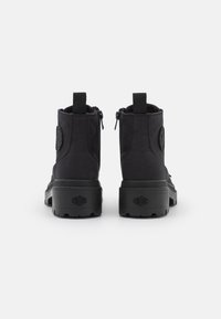 Bottines noires en toile avec tige en toile, fermeture éclair, talon renforcé et semelle en caoutchouc texturée présentant un logo distinct sur le côté.