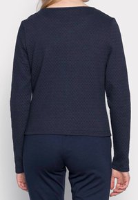 Top de manga larga color navy hecho de tejido texturizado, con cuello redondo y dobladillo recto. Mangas lisas sin patrones ni acentos.