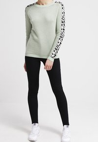 Mintgrüner, gerippter Pullover mit Leopardenmuster-Akzenten an den Ärmeln, kombiniert mit schwarzen Skinny Jeans und weißen Sneakers.