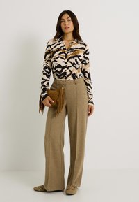 Blusa de manga larga y cuello con estampado animal en marrón y negro, combinada con pantalones de pierna ancha beiges y un bolso de mano de flecos en tono marrón.