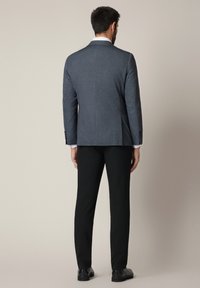 Szary żakiet o teksturowanym wykończeniu w dopasowanym fasonie, z czarnymi spodniami i skórzanymi butami, widoczny z tyłu.