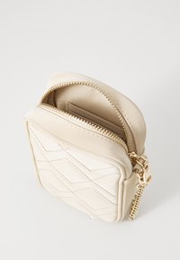 Béžová kožená taška s prošívaným vzorem, zlatým zipem a jemnou texturou. Uvnitř se nachází jedna přihrádka.