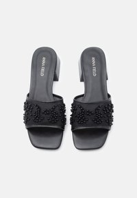 Sandales à glissière noires avec une bride texturée ornée de perles noires et de motifs floraux, dotées d'un petit talon carré et d'une semelle lisse.