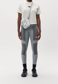 Grå träningsleggings med kontrasterande paneler, kombinerat med en ljusfärgad t-shirt med kort ärm och en liten grå crossbody-väska.