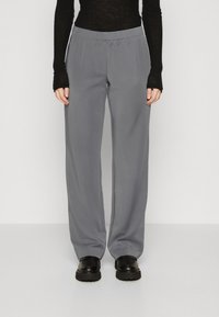 Pantalons larges gris en tissu lisse avec une taille élastique. Associés à un haut noir à manches longues et à des chaussures à plateforme noires.