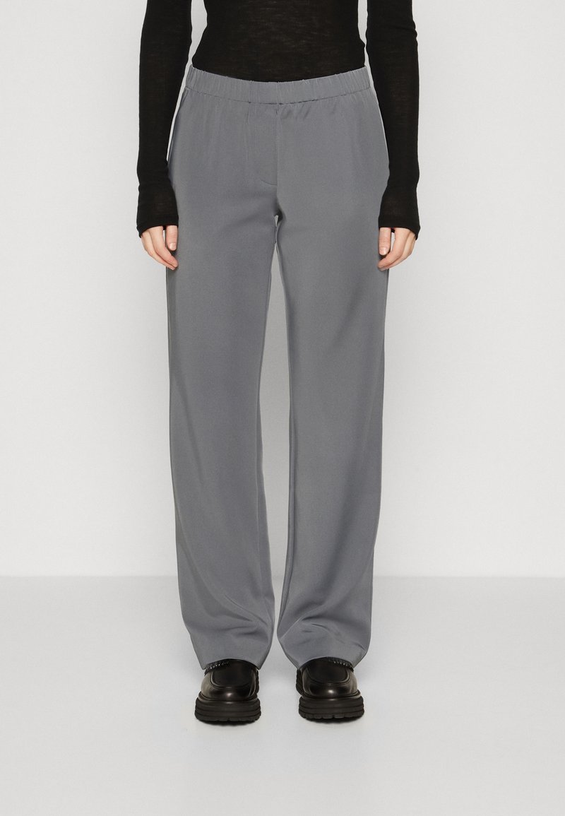 Pantalones de pierna ancha gris hechos de una tela suave con cintura elástica. Combinados con una camiseta negra de manga larga y zapatos de plataforma negros.