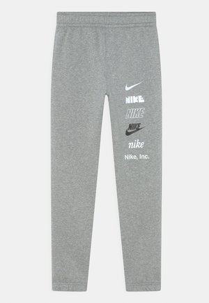 Graue Jogginghose mit elastischem Bund, die mehrere weiße und schwarze Nike-Logos sowie Text vertikal ausgerichtet am rechten Bein zeigt.