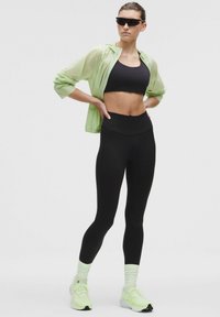 Svart kort topp, högmidjade svarta leggings, ljusgrön halvgenomskinlig jacka, svarta solglasögon och neongröna träningsskor med vita snören.