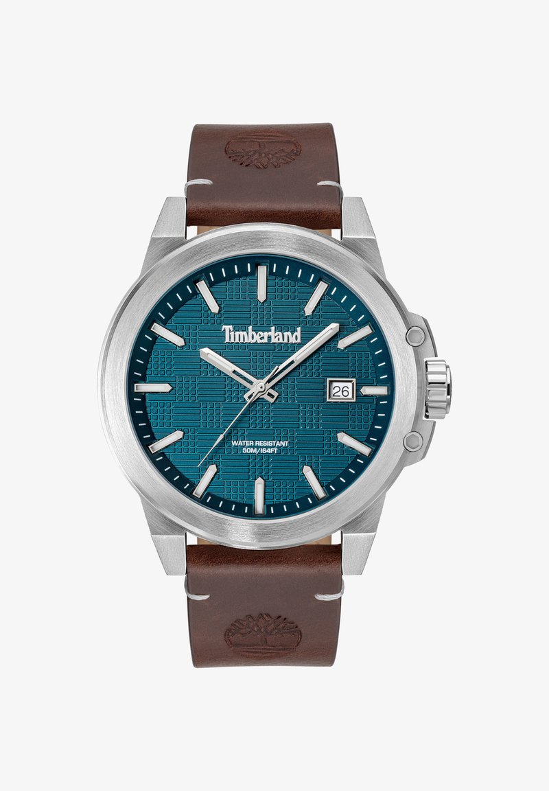 Orologio rotondo in acciaio inossidabile con quadrante teal e motivo in rilievo. Il cinturino in pelle marrone presenta un logo e contrasta con la cassa in metallo.
