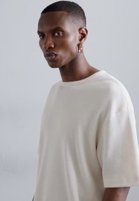 Cream ribbed short-sleeve T-shirt with a relaxed fit. Features a round neckline and soft texture. Worn with a clear accent earring.