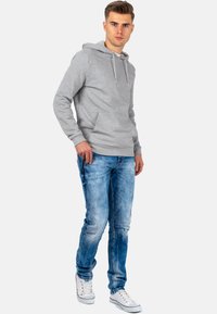 Sweatshirt à capuche gris en coton avec poche frontale, associé à un jean en denim délavé bleu clair et des baskets blanches. Design simple et décontracté.