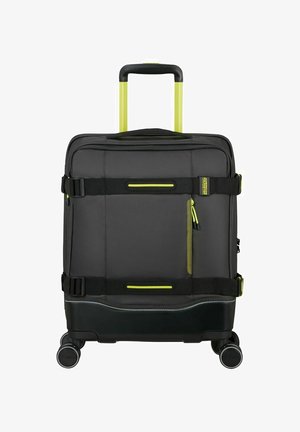 Maleta rígida negra con acentos amarillos, que cuenta con ruedas, un mango retráctil, un bolsillo frontal con cremallera y correas ajustables.