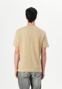 T-shirt en coton kaki avec un col rond et des manches courtes, présentant un design simple et une texture lisse, vu de l'arrière.
