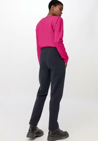 Fuchsiová košile s dlouhým rukávem a volným střihem, doplněná tmavě šedými tapered tepláky. Černé kotníkové boty dokončují outfit.