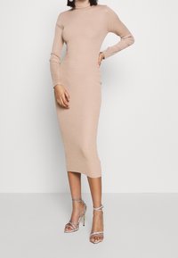 Robe midi en tricot beige clair avec des manches longues, texture côtelée et silhouette ajustée. Associée à des sandales à talons hauts argentées à brides.