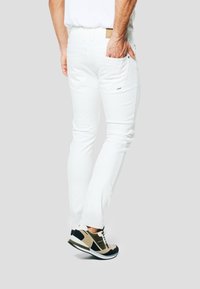 Vaqueros blancos de algodón con un diseño de corte slim, que cuentan con bolsillos traseros y detalles de costura sutiles, combinados con zapatillas negras y beige.