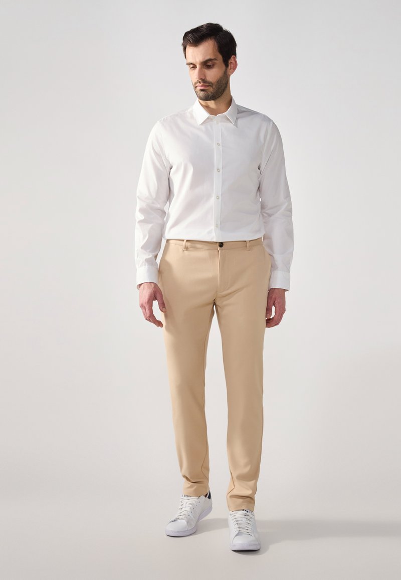 Lightweight beige trousers with a straight leg design, paired with a white button-up shirt and white sneakers. Smooth fabric texture.