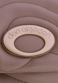Material de cuero topo con un patrón acolchado; presenta un prominente logotipo ovalado de hardware dorado grabado con "don algodon."