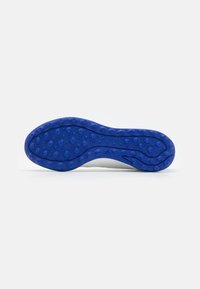 Suela de zapato que presenta un material de goma azul texturizada con patrones circulares, en contraposición a una sección superior blanca y una forma aerodinámica.