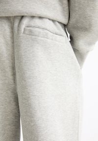 Graue Sweatpants aus weichem Stoff mit einer Seitentasche und einer lockeren Passform, die eine glatte Textur und minimale Nähdetails aufweisen.
