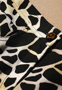 Tessuto nero e beige con motivo a stampa giraffa, caratterizzato da materiale texturizzato e dettaglio di un bottone bronzo sulla vita.