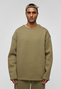 Overgrote olijfgroene sweatshirt, ronde hals, lange mouwen, zachte textuur, minimale naden, gecombineerd met bijpassende broek.
