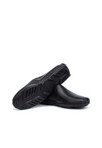 Los zapatos negros de piel sin cordones presentan una punta redondeada, detalles cosidos y una suela de goma texturizada con patrones de relieve para mayor agarre.
