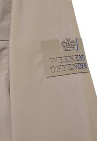 Beige jacket featuring a textured fabric and a prominent silver and blue logo patch reading "WEEKEND OFFENDER" with a crown accent.