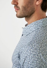 Hemd met knoopjes in een blauw-wit geometrisch patroon, met kraagontwerp en zichtbare textuur, waarbij een casual stijl wordt benadrukt.