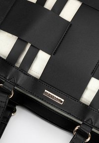 Tote tissé noir avec un tissu blanc contrasté en dessous. Comprend des accents en cuir lisse, du matériel doré et un design de poignées entrelacées.