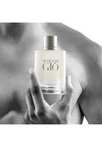 Une personne torse nu tient une bouteille de parfum Acqua di Giò givrée de Giorgio Armani devant sa poitrine.