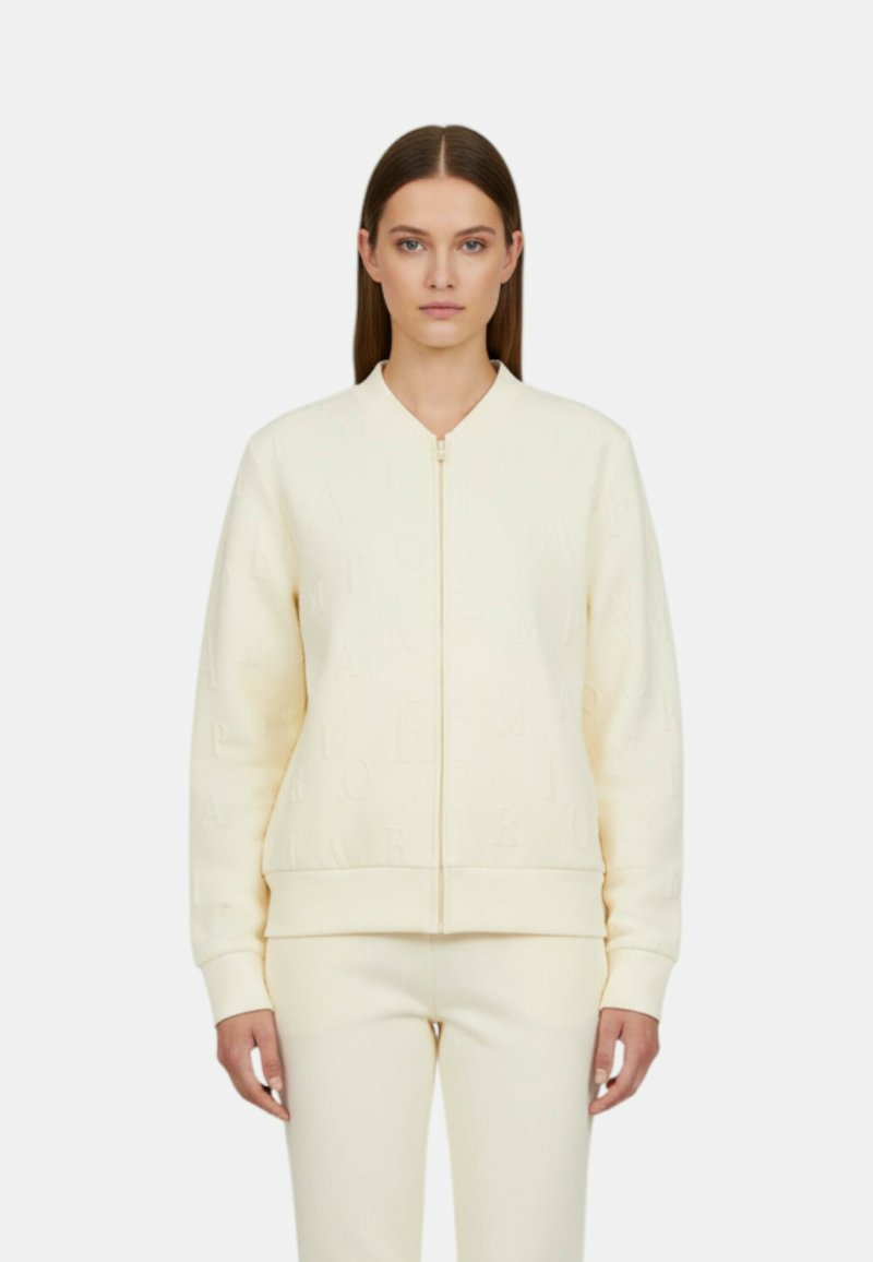 Felpa crema con zip e lettere in rilievo, polsini e orlo a coste, tessuto leggero e vestibilità ampia con pantaloni coordinati.