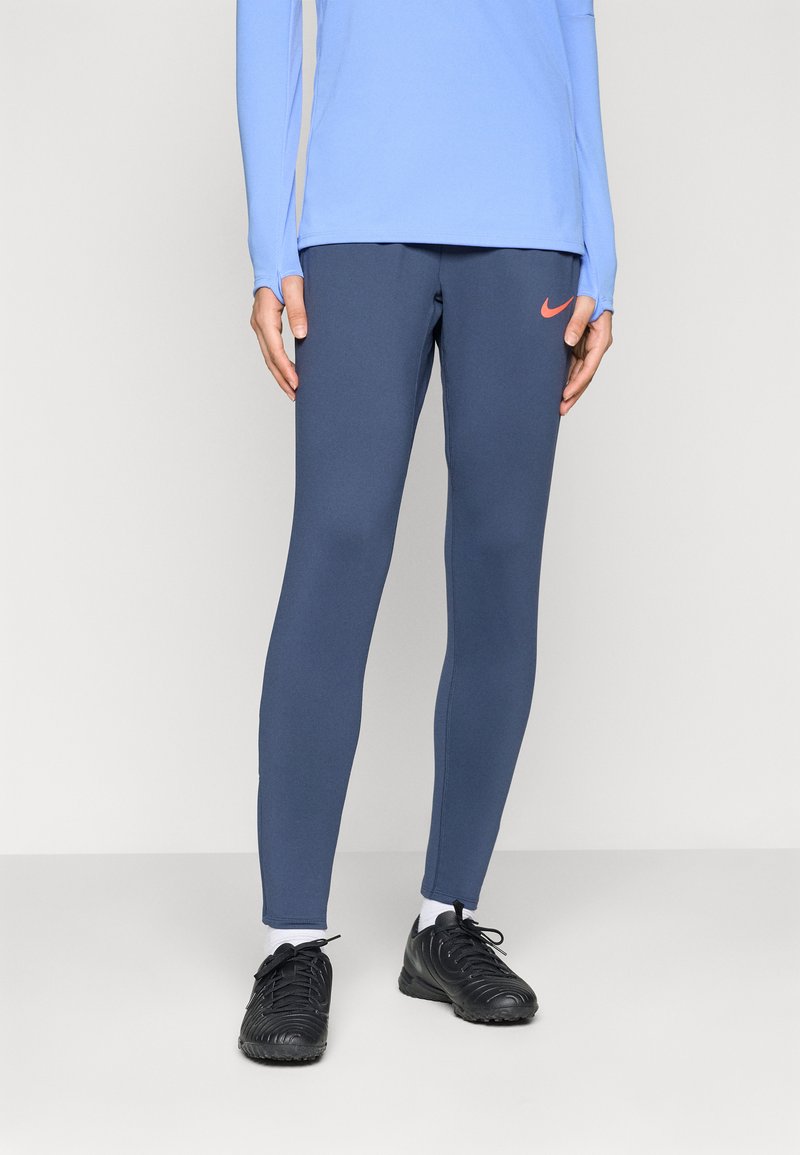 Leggings de couleur marine en tissu extensible, avec une coupe ajustée et un petit logo Nike orange sur la cuisse gauche.