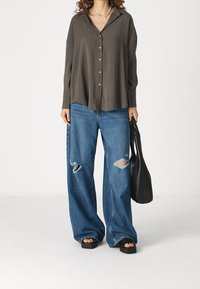 Camicia button-up oversize in carbone, jeans a gamba larga in denim chiaro sbiadito, sandali neri piatti e una borsa a tracolla nera. Tessuto leggero e vestibilità comoda.