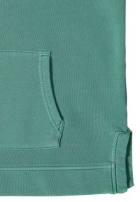 Tela de color verde azulado con un bolsillo frontal rectangular y costuras visibles, mostrando la parte inferior de una prenda.