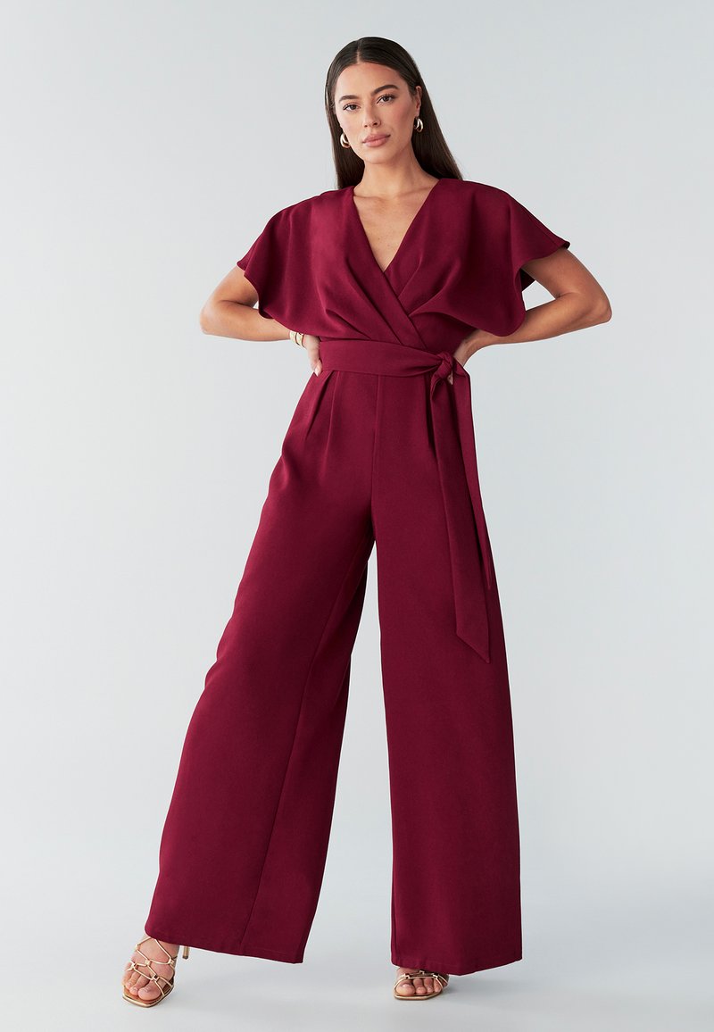 Mono burdeos con escote en V, mangas cortas tipo kimono y cintura con cinturón. Diseño de pierna ancha hecho con tela suave sin patrones visibles.