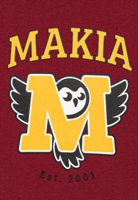 Maroon T-skjorte med gul tekst "MAKIA" og et stort gult "M" med en ugle og vinger design, samt "Est. 2001" i svart.