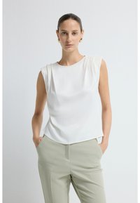 Hvid ærmeløs top med en afslappet pasform, blød tekstur og let fald; parret med lysegrønne skræddersyede bukser.