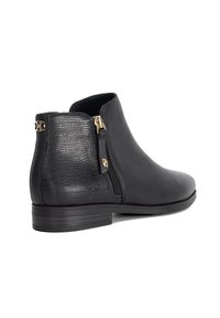 Black leather ankle boot with textured heel, gold zipper and decorative gold emblem on the back, low stacked sole.