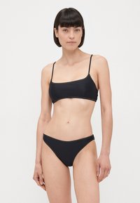 Crni bikini set s tankim trakama. Gornji dio ima kvadratni izrez i elastičan materijal. Donji dio ima nisku siluetu s kontrastnim šavovima.