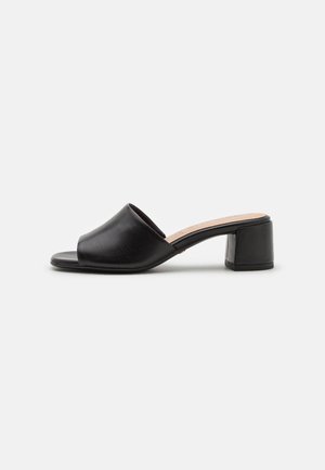 Black leather mules with an open toe design, low block heel, and smooth texture. Features a simple, curved upper and flat sole.